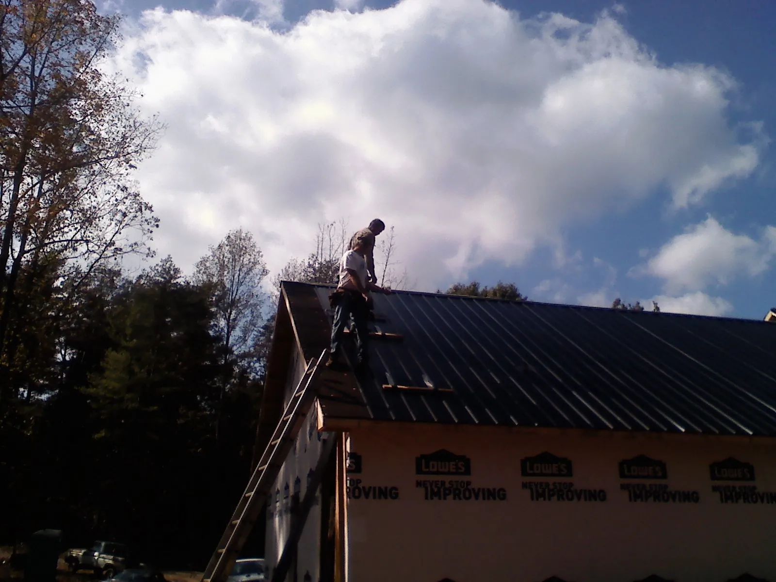Roofer fastening dark metal panels high against a cloudy sky, from a Roof Inspection job in Snoqualmie