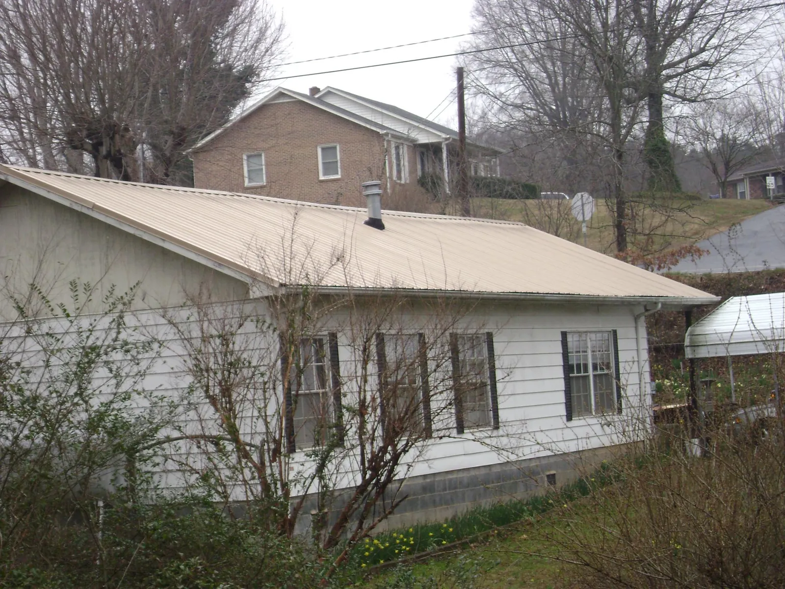 Tan metal roof on a white sided house set into a hillside — Commercial Roofing by Roofing Brothers in Snoqualmie